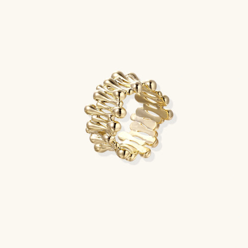 Gold-plated brass ring with sculptural petal-like elements in a wide band design on beige background