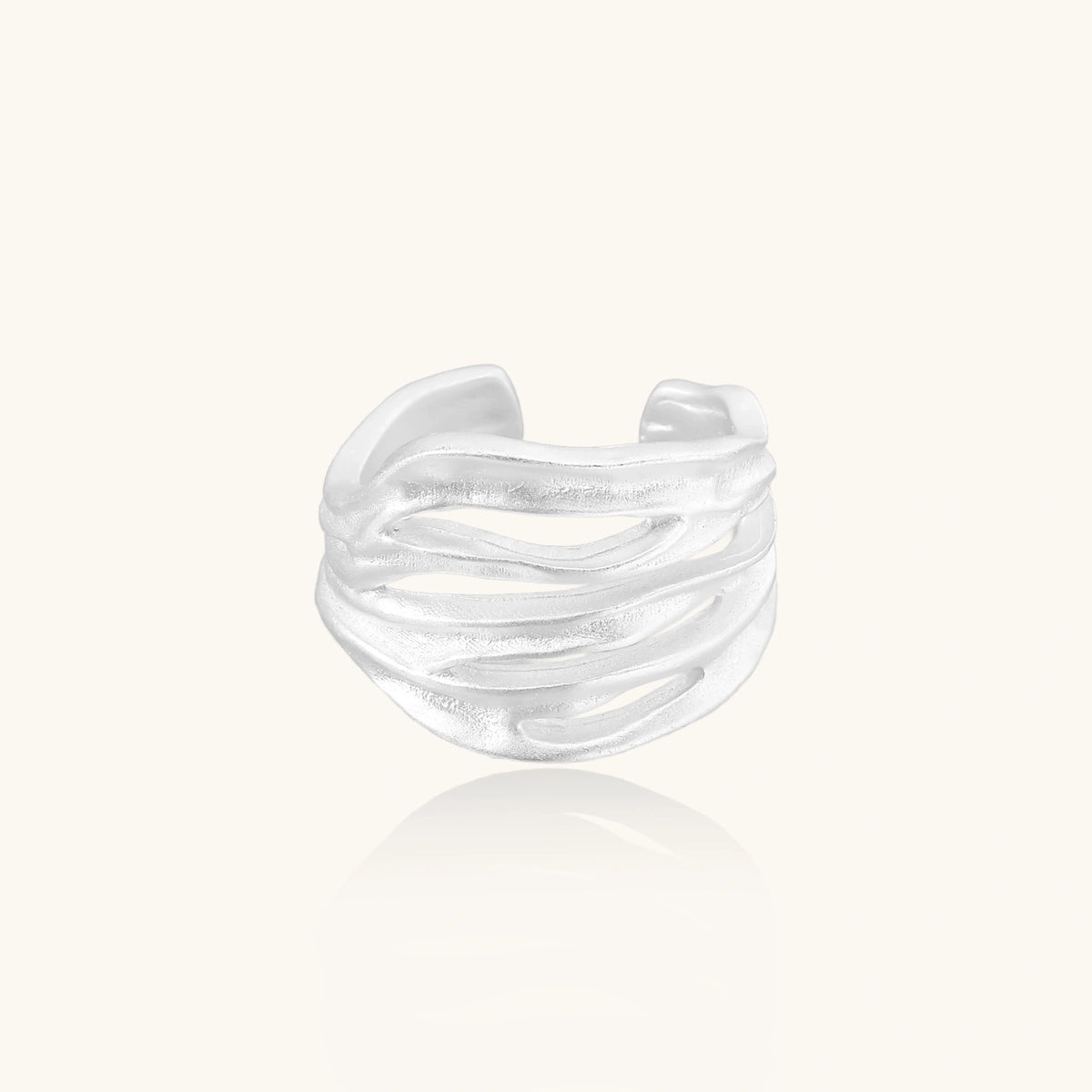 Wide sterling silver cuff ring with flowing wave patterns creating dimensional texture against cream background