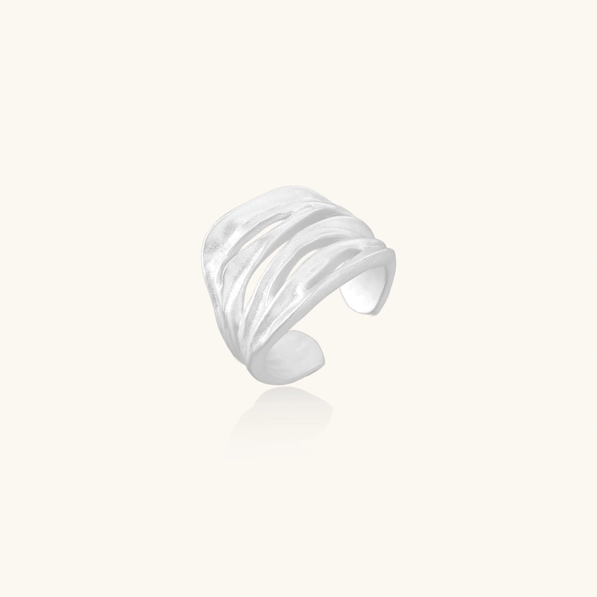 Wide sterling silver cuff ring with flowing wave patterns creating dimensional texture against cream background