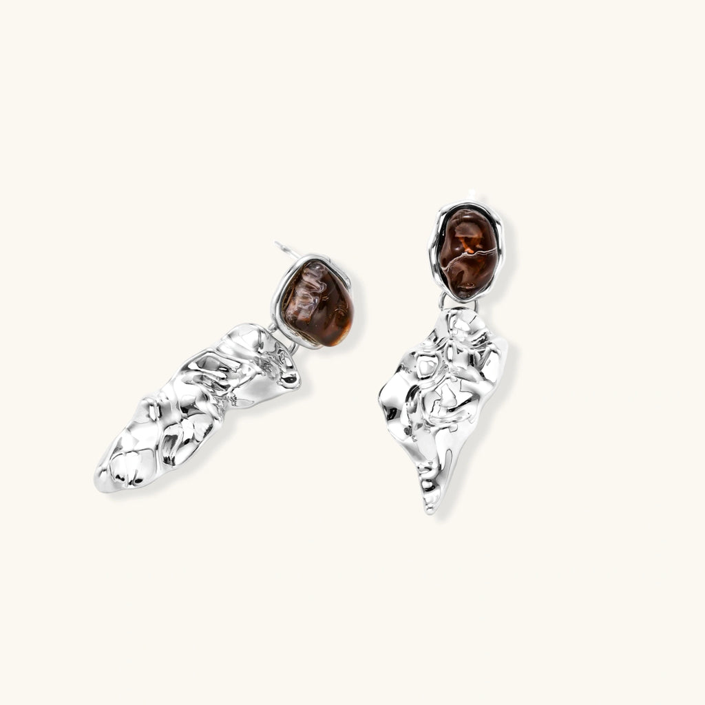 Abstract sculptural silver earrings with brown resin stones featuring organic fluid metalwork design on white background.
