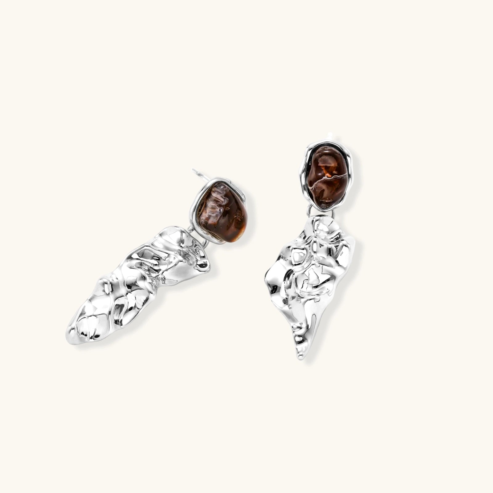 Abstract sculptural silver earrings with brown resin stones featuring organic fluid metalwork design on white background.