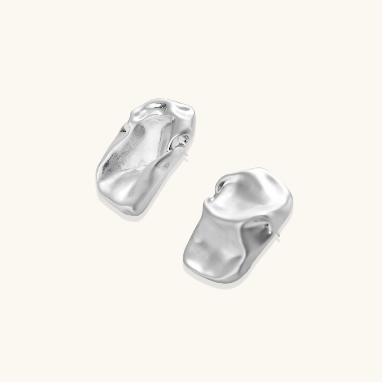 Pair of sculptural silver ear cuffs with organic fluid shapes and polished finish against cream background.