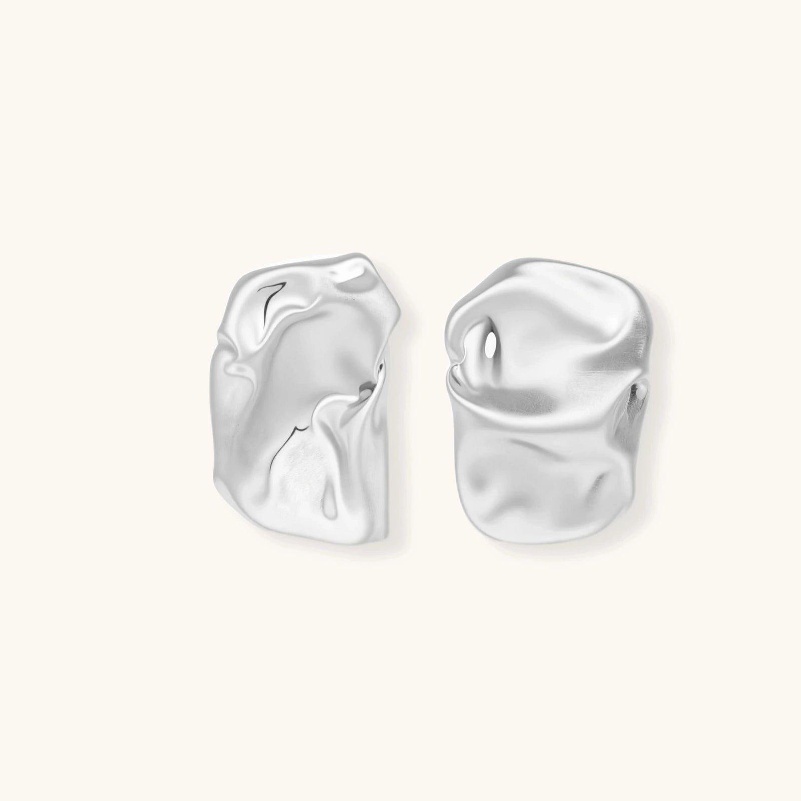 Pair of sculptural silver ear cuffs with organic fluid shapes and polished finish against cream background.