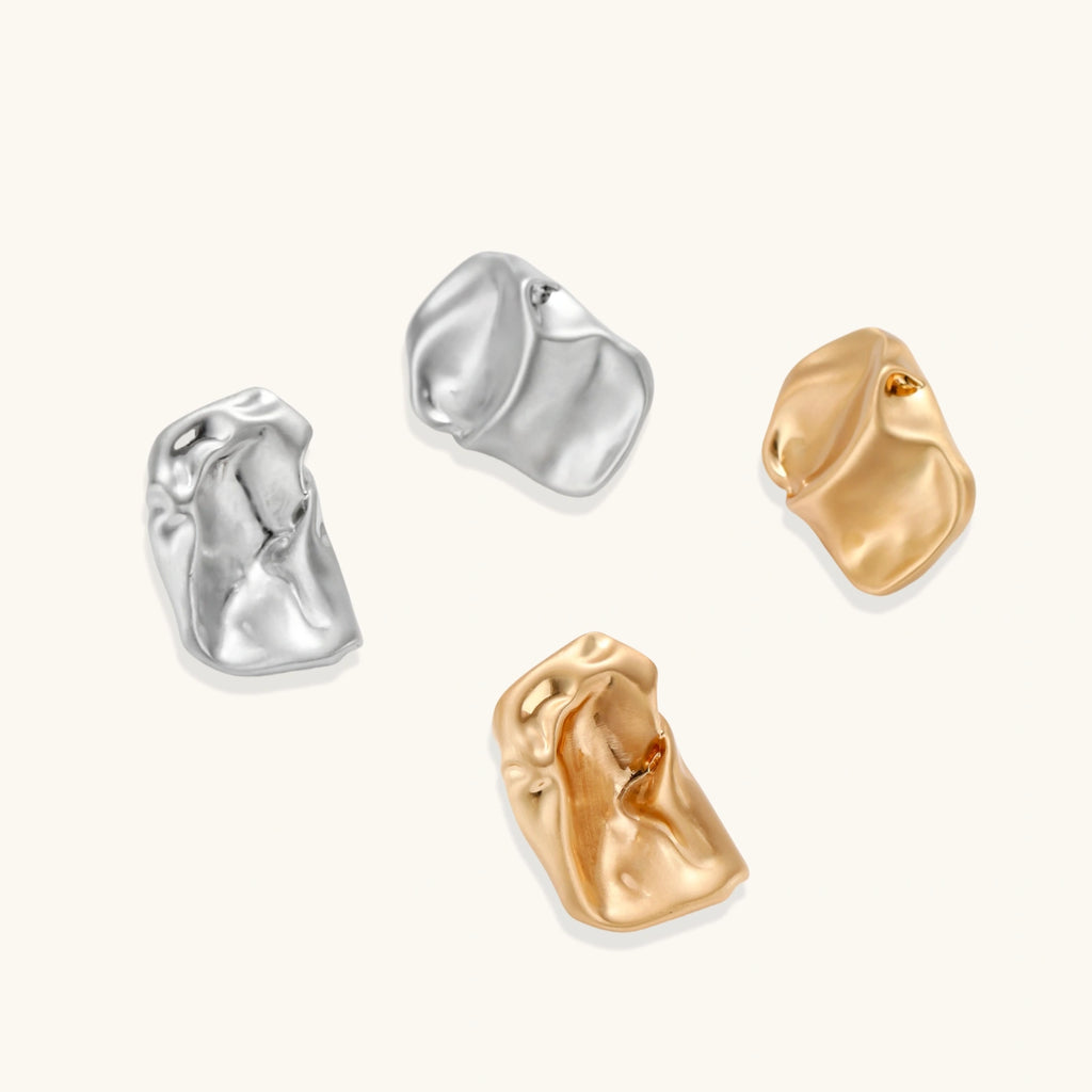 Pair of sculptural silver ear cuffs with organic fluid shapes and polished finish against cream background.