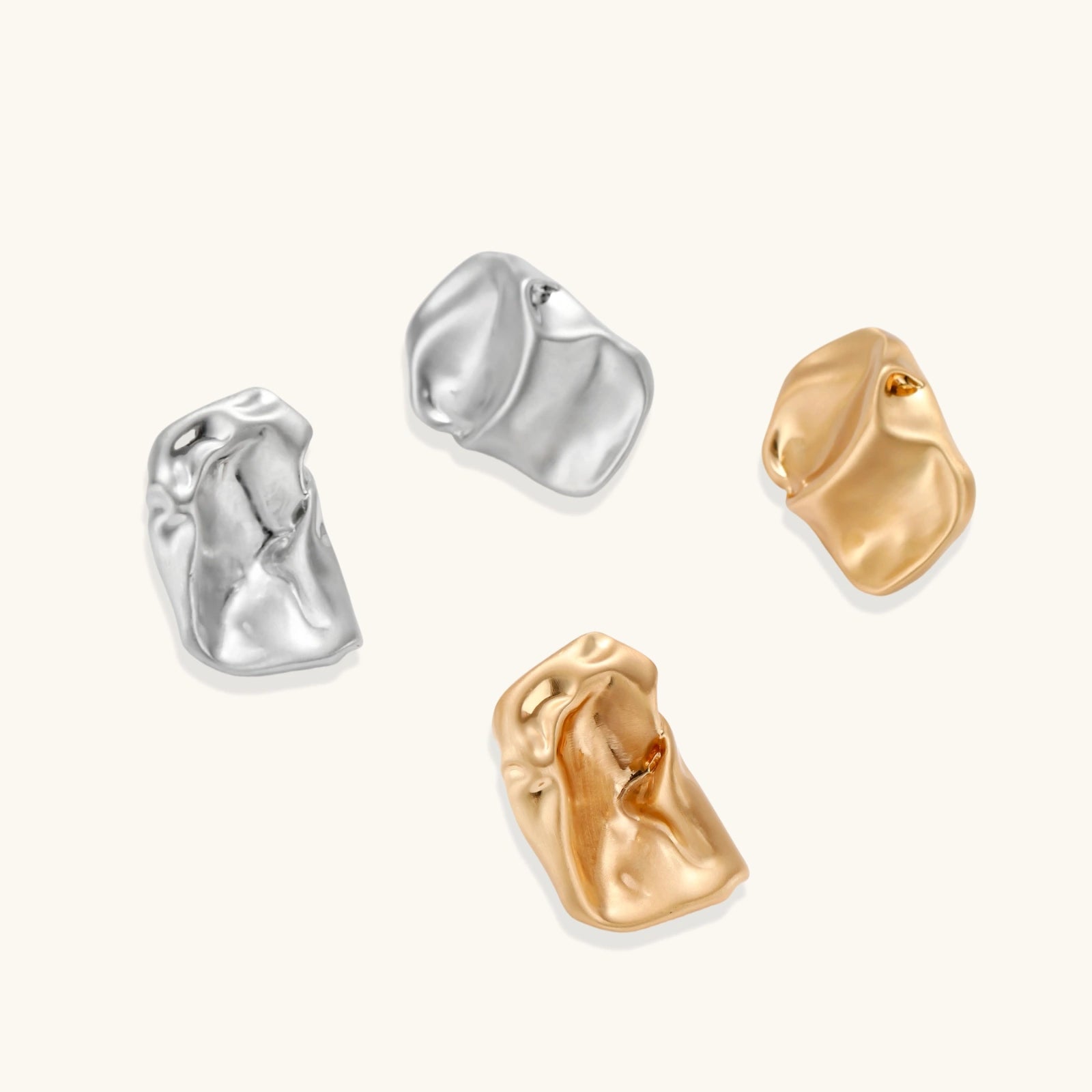 Pair of sculptural silver ear cuffs with organic fluid shapes and polished finish against cream background.